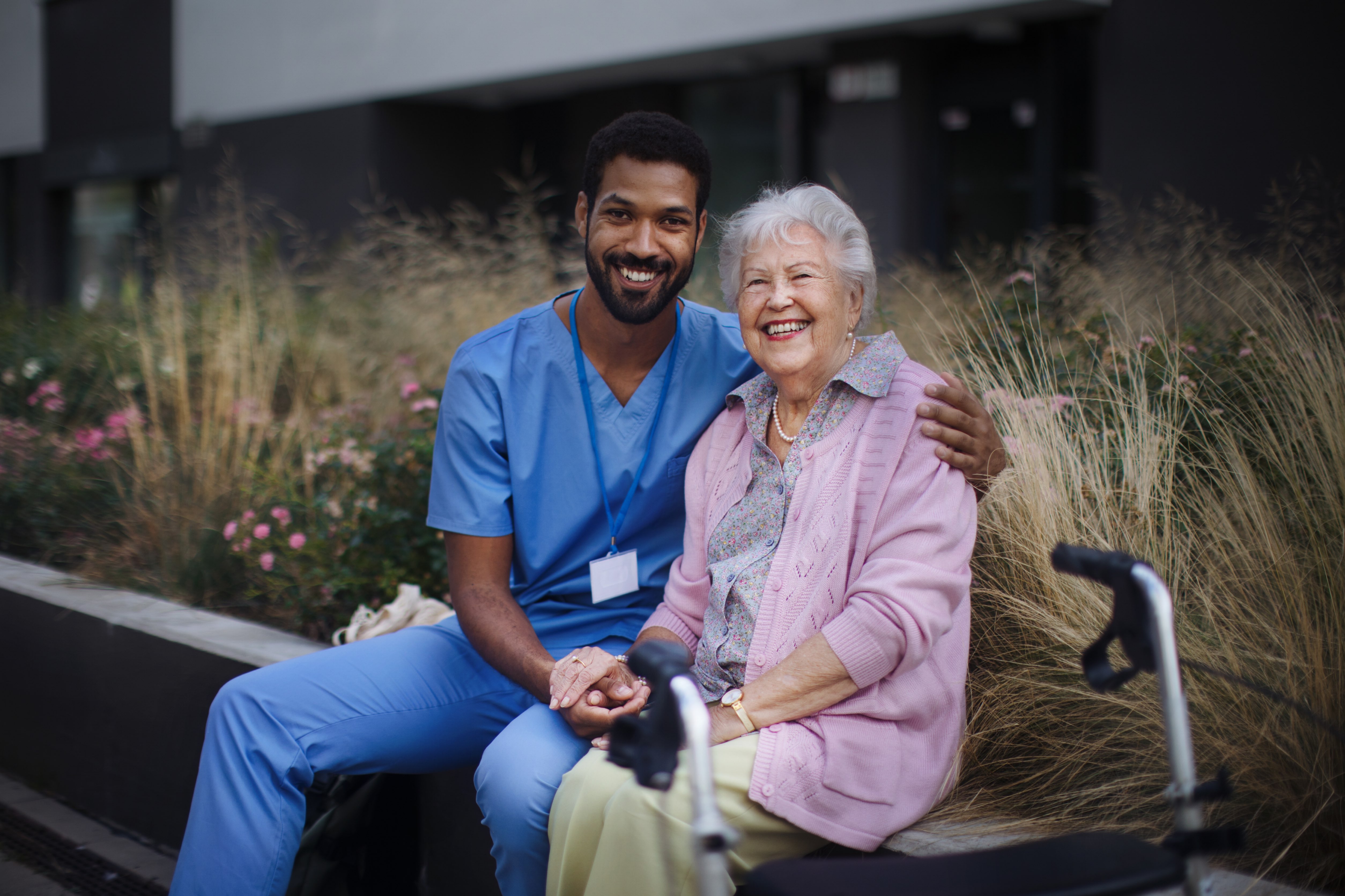 Smiling nurse sitting beside an elderly woman during outdoor assisted living visit.