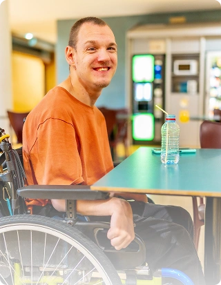 Smiling man in a wheelchair sitting at a table in a care facility