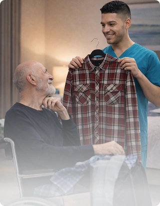 Caregiver showing a shirt to an elderly man in a wheelchair during assisted daily care