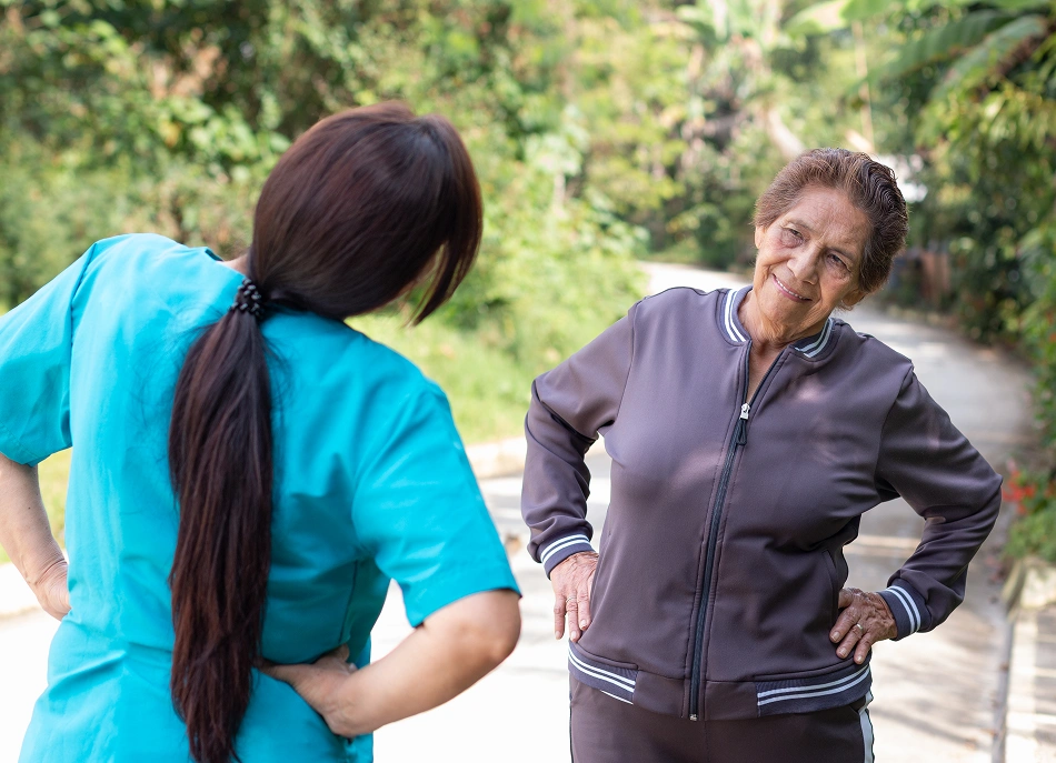 Caregiver and senior woman stretching together outdoors.