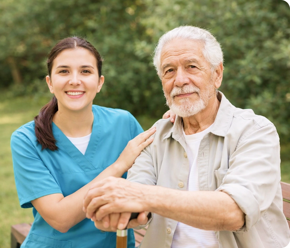 Caregiver sitting with an elderly man outdoors on a bench.
