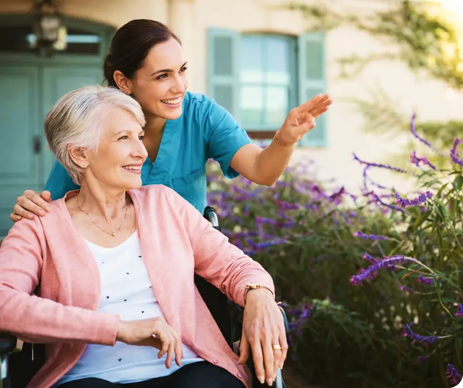 Caregiver with a senior woman in a wheelchair outdoors by flowers.
