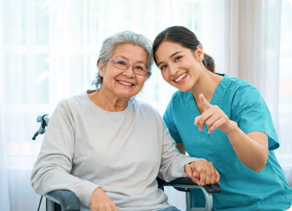 Smiling caregiver sitting with an elderly woman in a wheelchair.
