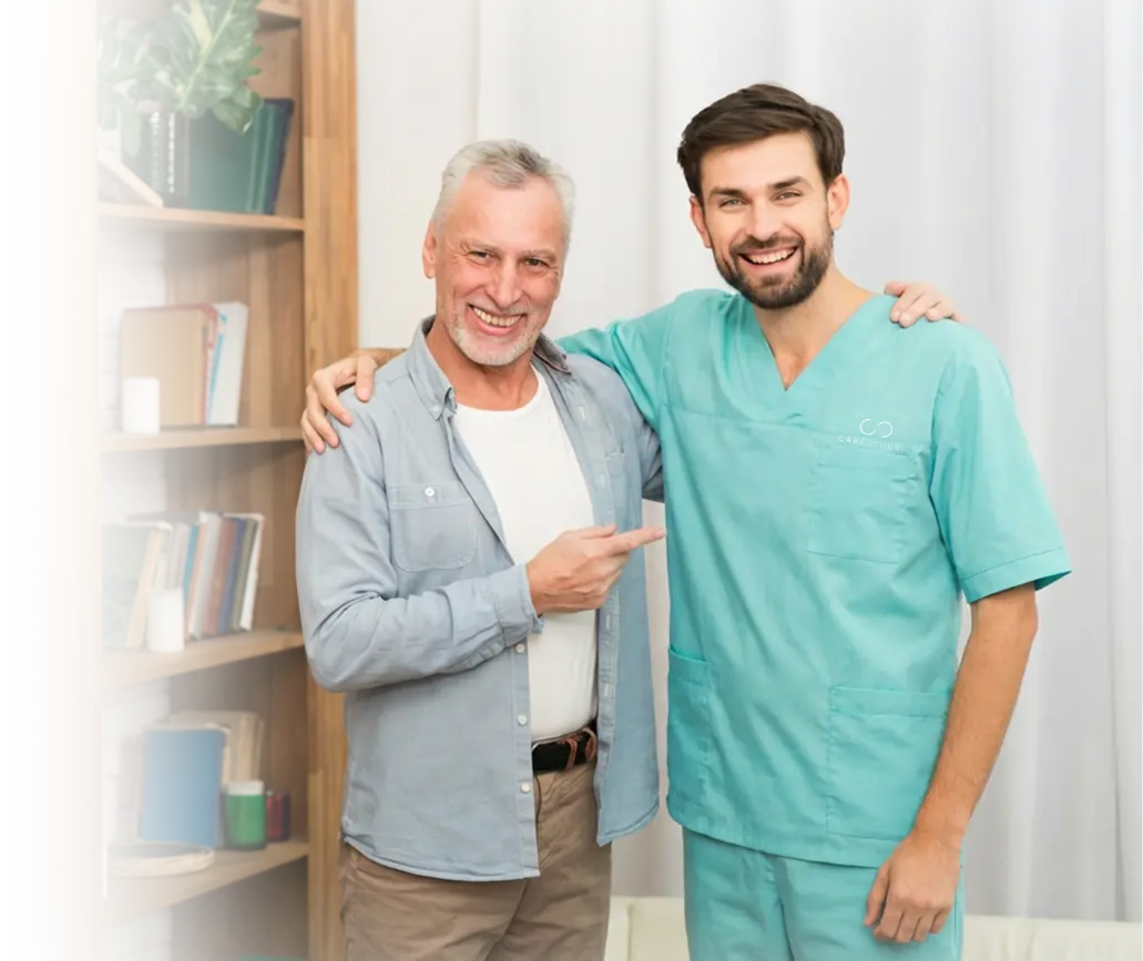 Smiling elderly man with his arm around a caregiver in teal scrubs indoors