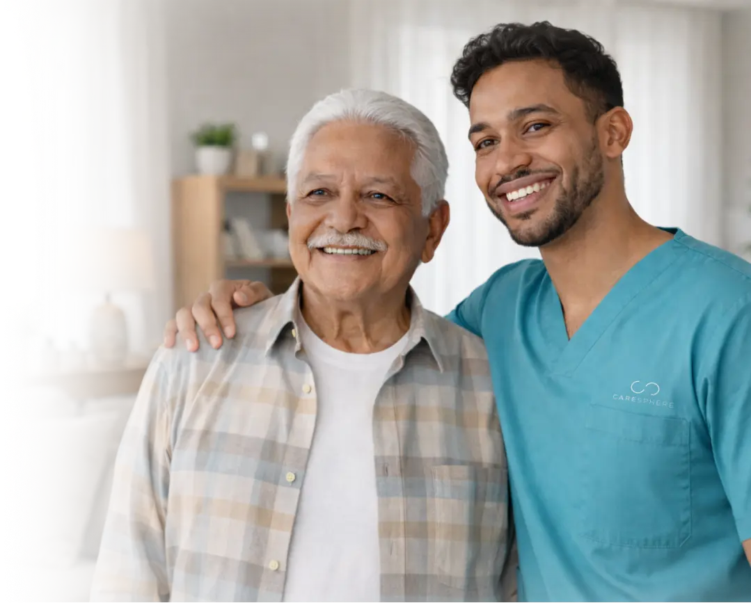 Smiling caregiver in teal scrubs with his arm around a cheerful elderly man indoors
